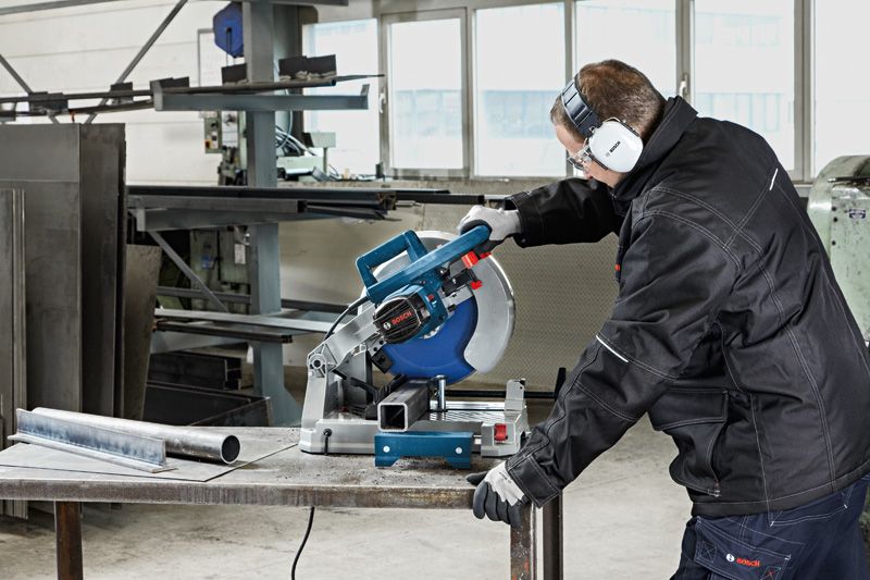 A person wearing safety equipment cuts a metal pipe with a metal cut-off saw.