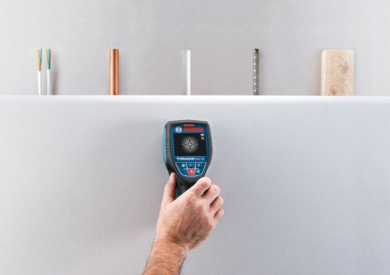 A person uses a wallscanner detector to locate hidden materials inside a wall.