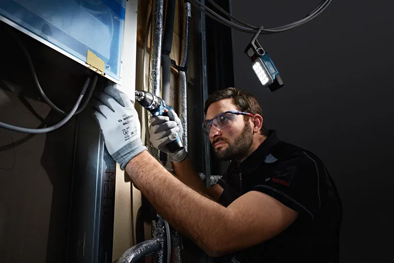 一名佩戴安全設備的人正在牆上鑽孔，無線燈照亮了工作空間。.