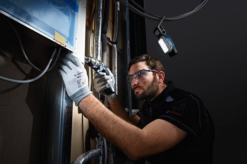 一名穿戴安全裝備的人員在LED工作燈下使用無線電鑽。