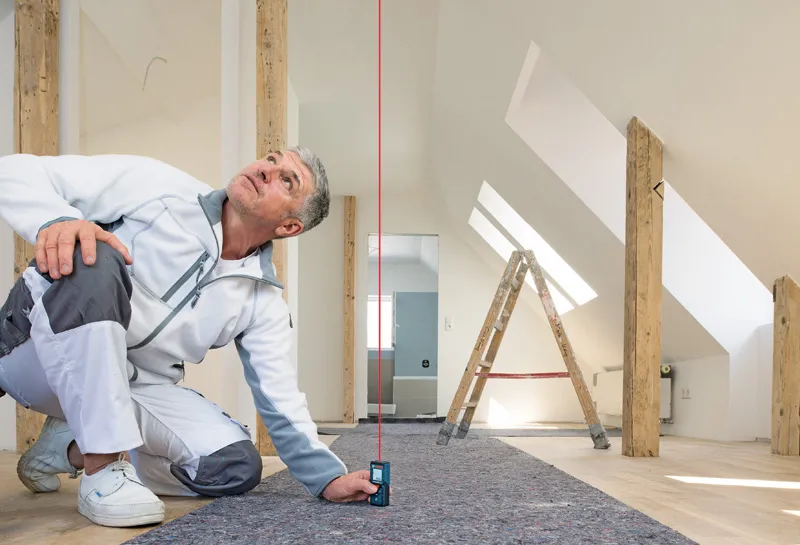A person uses a laser measure to check alignment in a room under construction.