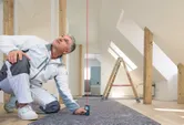 A person uses a laser measure to check alignment in a room under construction.