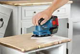A person operates a cordless power sander on a flat surface.