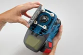 A person opens the base plate of a blue handheld power tool.