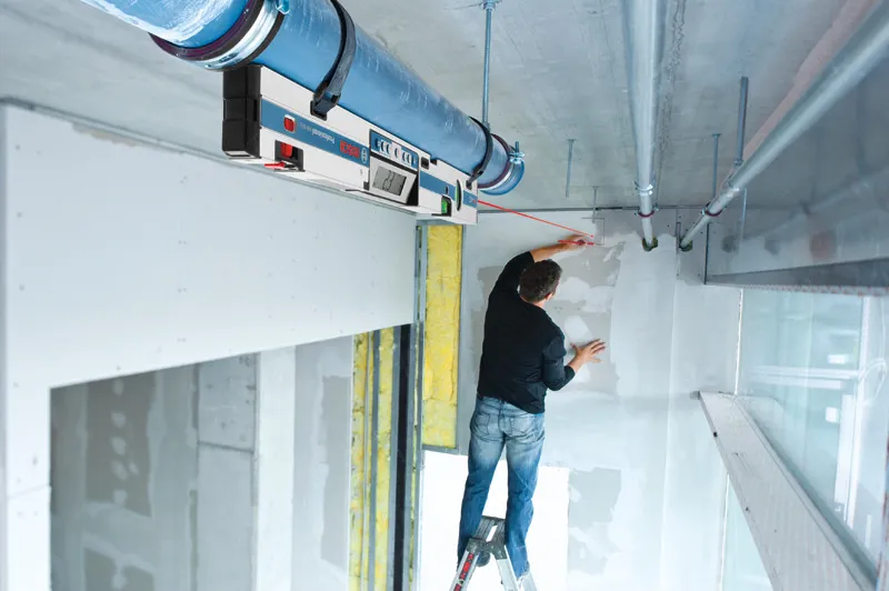 一個人站在梯子上，用數位測斜儀在牆上做標記，以便對準。.