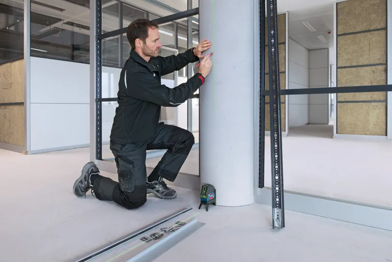 一名佩戴安全設備的人員正在使用雷射調平工具標記混凝土柱。.