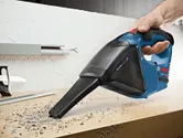 一個人使用無線吸塵器清理工作台上的碎屑。