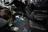 一名配戴安全設備的人員正在使用無線吸塵器清潔汽車地板。