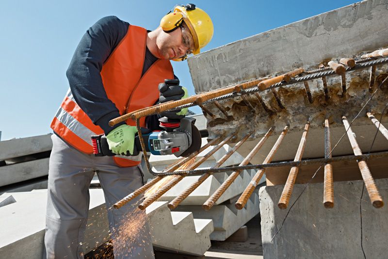 在建築工地上，一名配戴安全設備的工人正在用電動工具切割突出的鋼筋。.