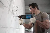 一名配戴安全設備的人員使用電動工具在混凝土牆上鑽孔。