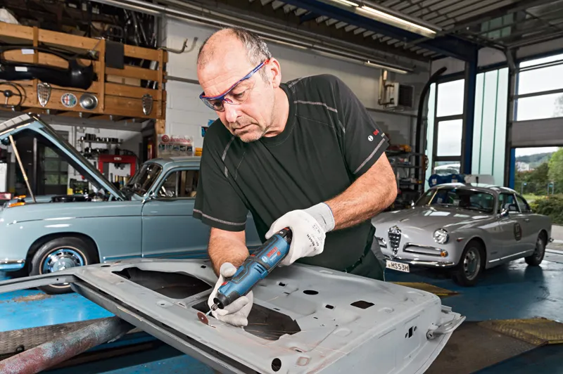 一名配戴安全設備的人員在車庫中使用無線旋轉工具研磨金屬。.