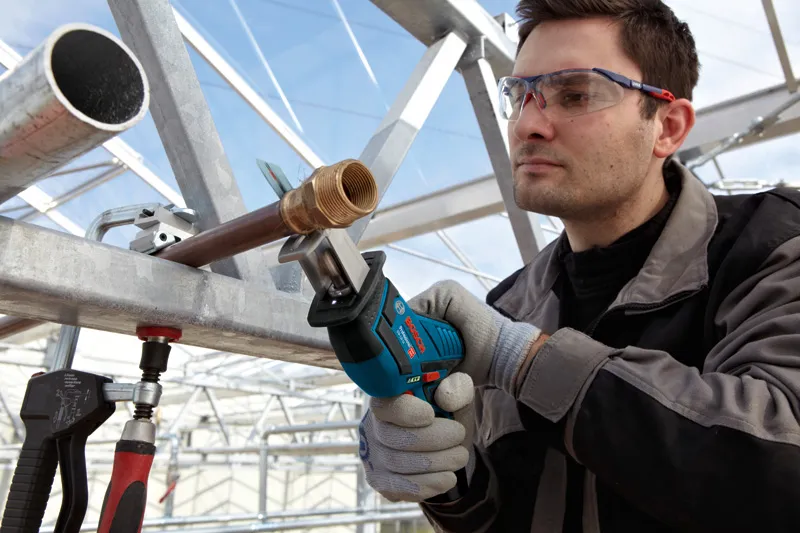 一名配戴安全設備的人員使用無線往復鋸切割金屬管路。.