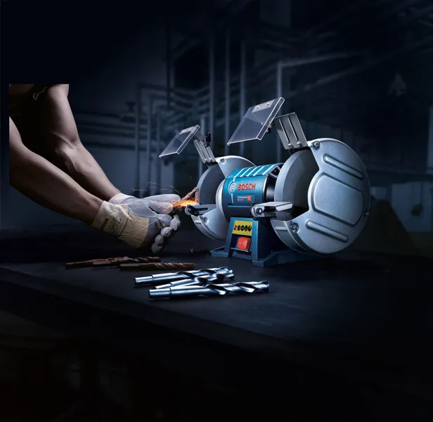 一名配戴安全設備的人正在用雙輪台式砂輪機磨鑽頭。