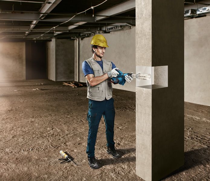 一名穿戴安全裝備的人員正在建築工地鑽探混凝土柱。