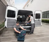 兩名工人在一輛敞篷貨車旁準備工具，其中一人正在操作無線吸塵器。