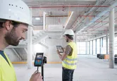 兩名配戴安全設備的人員在大型建築工地內使用雷射測量儀和平板電腦。