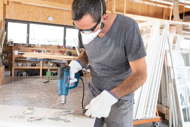 一名配戴安全設備的人員使用熱風槍去除表面的油漆。