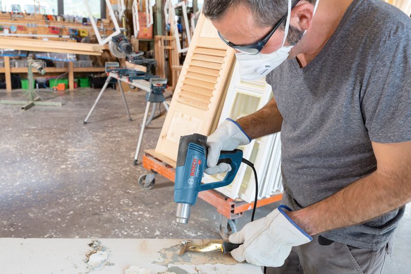 一名配戴安全設備的人員使用熱風槍去除木質表面的油漆。