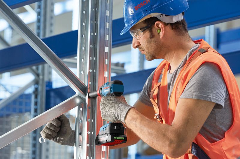 一名配戴安全設備的人員使用無線電鑽固定金屬框架。.