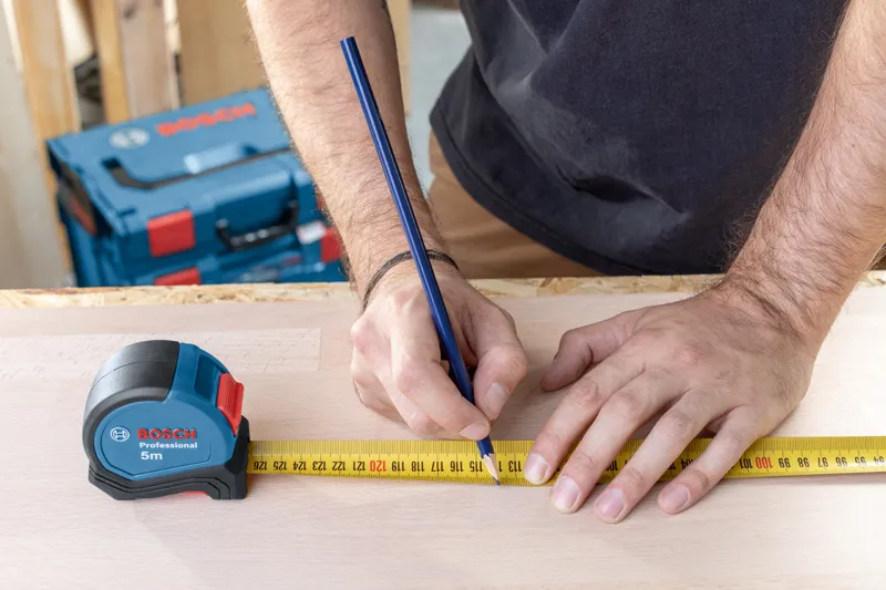 捲尺5 m 一個人用捲尺和鉛筆在木頭上標記測量值。.