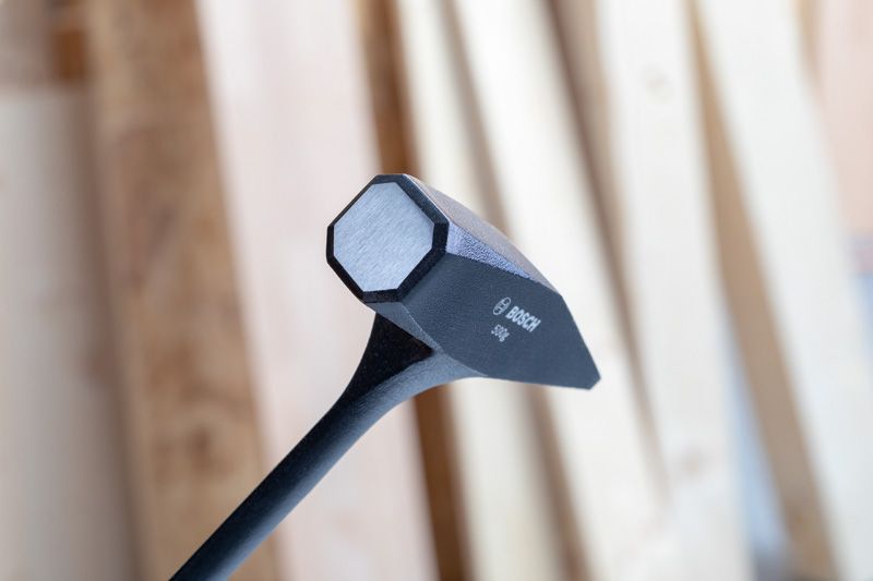 黑色大鎚頭，具有扁平的打擊面，在模糊的木質背景下呈現。.