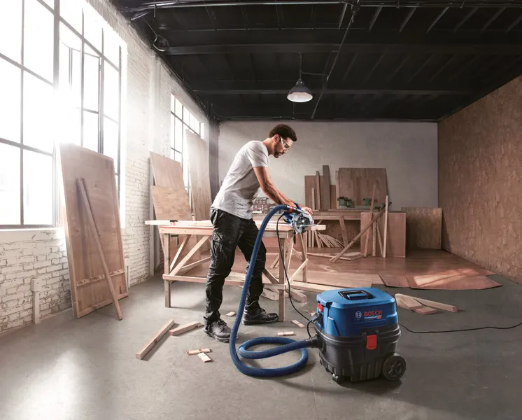 一名配戴安全設備的人員在木材車間使用吸塵器。.