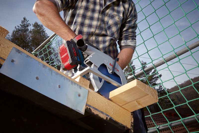 A person cuts a wooden beam with a circular saw at a construction site.