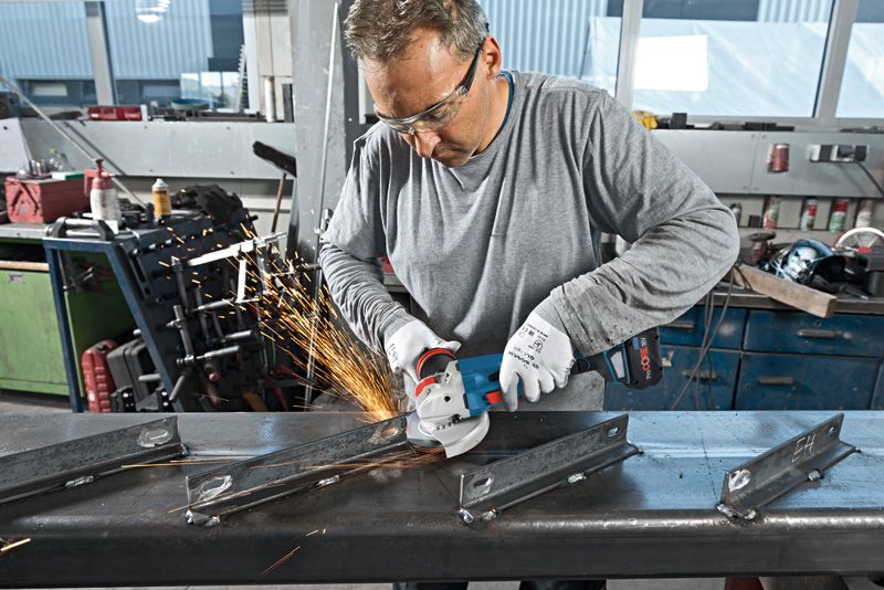 一名配戴安全設備的工人使用無線角磨機打磨金屬梁。.