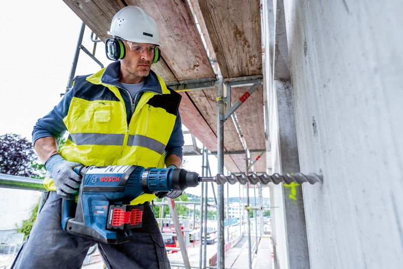 一名佩戴安全設備的人員使用無線旋轉錘在混凝土中鑽孔。.