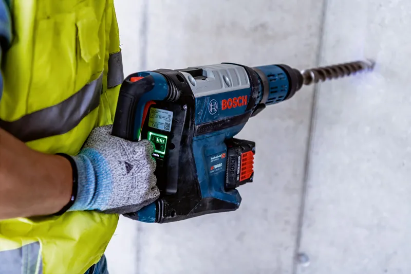 一名佩戴安全設備的人員使用大型旋轉錘在混凝土中鑽孔。.