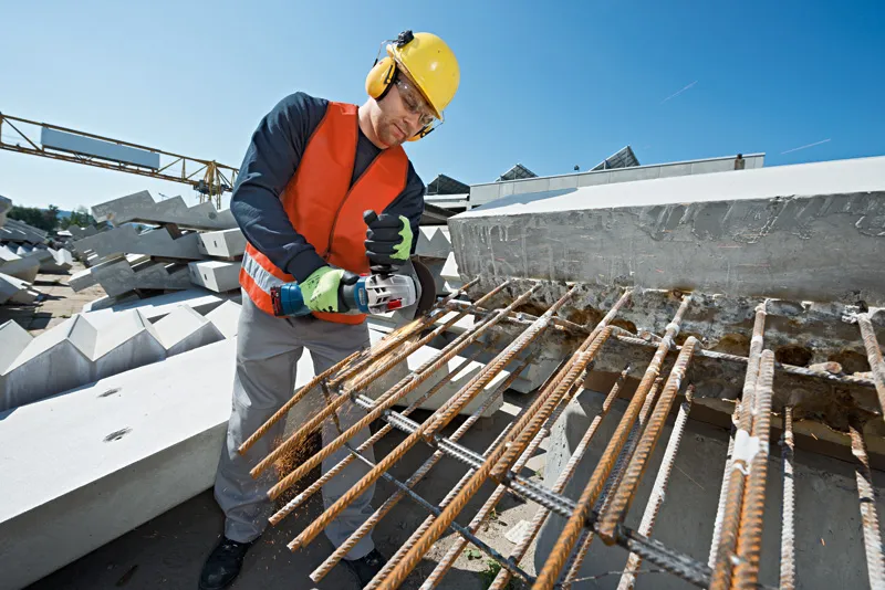 在建築工地上，一名配戴安全設備的工人正在用電動工具切割鋼筋。.