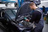 在汽車修理廠，一名工作人員正在使用熱成像儀檢查汽車引擎。