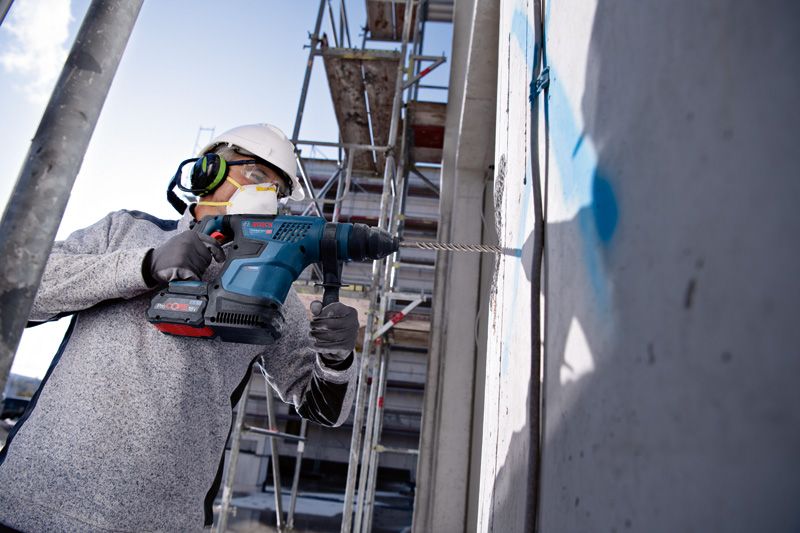 一名戴著安全設備的工人在建築工地上鑽入混凝土牆。.