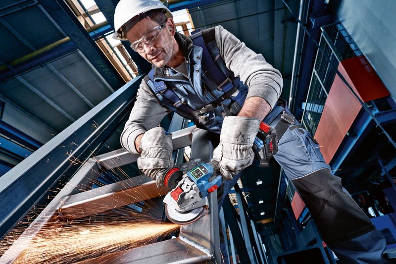 GWX 18V-15 SC 一名配戴安全設備的人用電動工具研磨金屬梁,產生火花。.