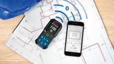 Laser measure and smartphone displaying measurements on architectural plans.