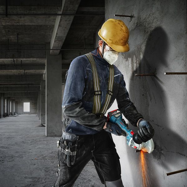 A person wearing safety equipment cuts concrete with an angle grinder.