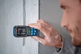 Person measuring a wall surface with a laser measure.