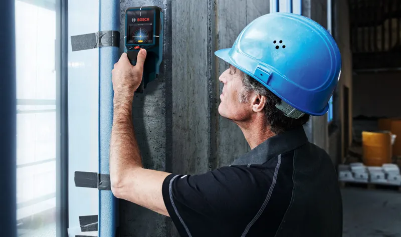 A person wearing safety equipment scans a concrete wall with a detector.