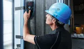 A person wearing safety equipment scans a concrete wall with a detector.