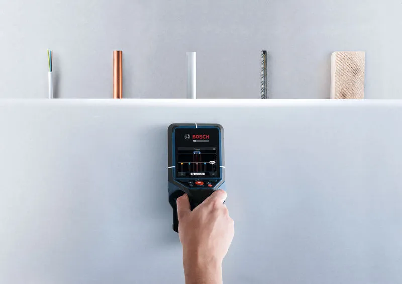 Person using a wall scanner detector to identify objects hidden behind a surface.