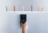 Person using a wall scanner detector to identify objects hidden behind a surface.