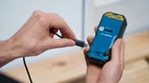 一個人將充電線連接到手持電動工具的背面。.