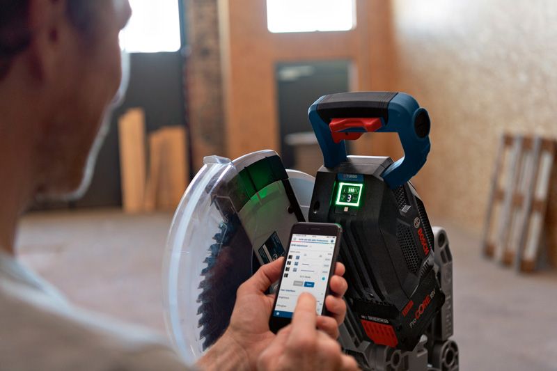 一名工人在室內車間使用智慧型手機調整無線斜切鋸。.