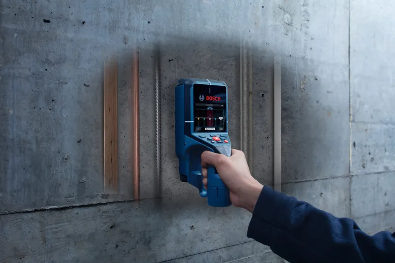 A person scans a concrete wall with a detector revealing hidden pipes and wiring.
