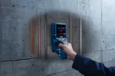 A person scans a concrete wall with a detector revealing hidden pipes and wiring.
