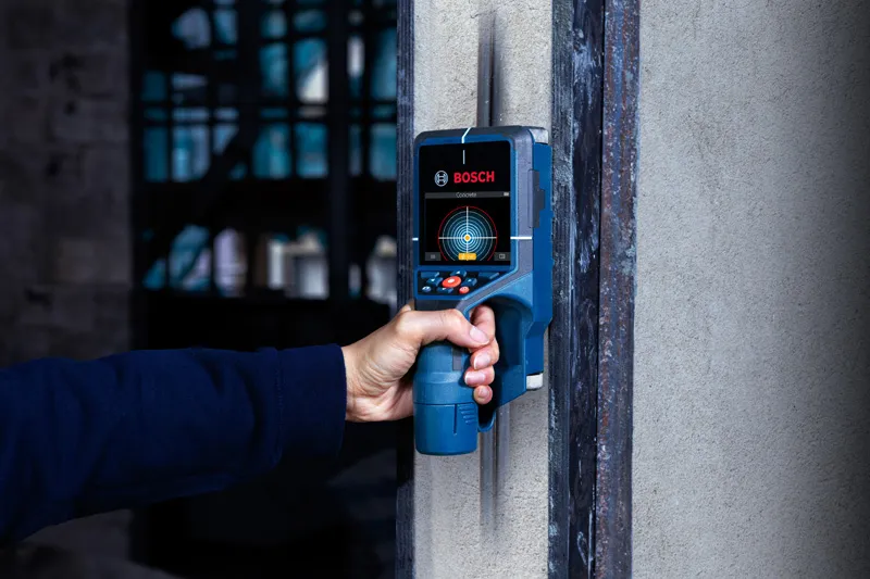 A person uses a digital wall detector to scan for objects inside a concrete wall.