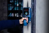 A person uses a digital wall detector to scan for objects inside a concrete wall.
