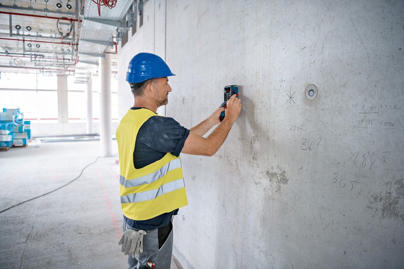 A person wearing safety equipment scans a concrete wall with a detector.