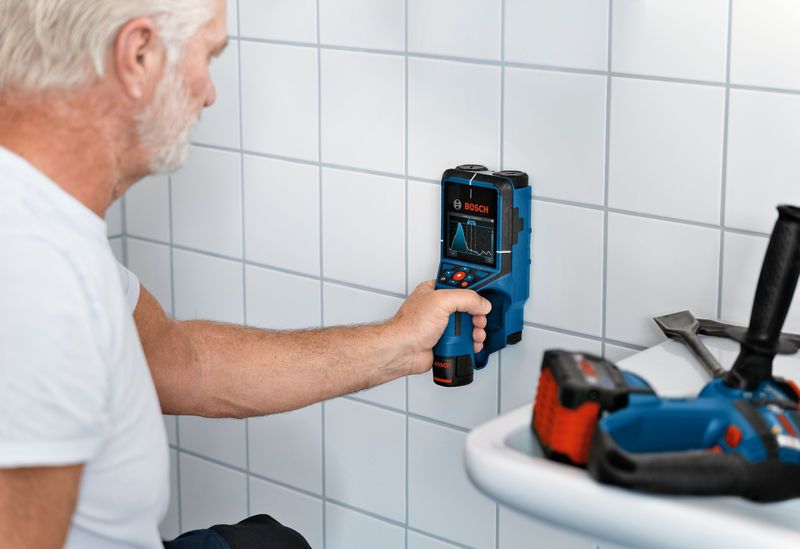 Person scans a tiled wall with an inspection tool in a workspace.