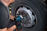 一名佩戴安全裝備的人員使用無線衝擊扳手來擰緊卡車車輪上的輪轂螺母。